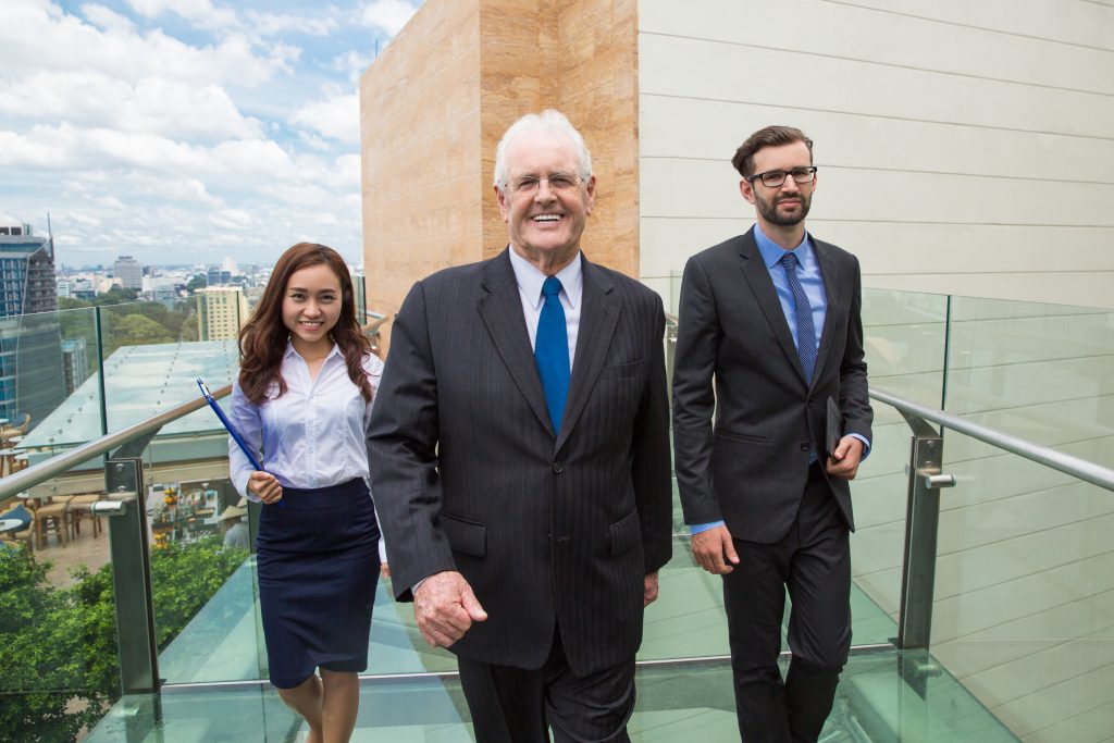 senior business man walking terrace followed by man woman